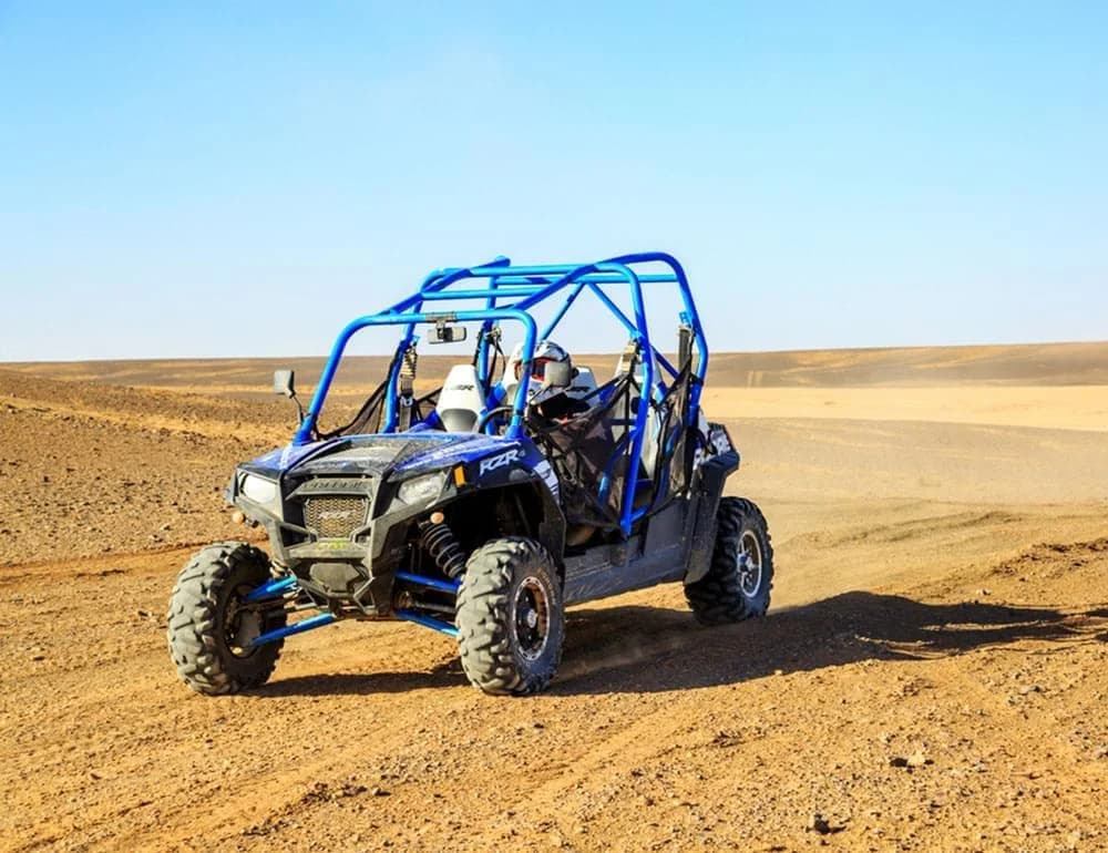 Two riders in helmets driving a buggy across the rocky Agafay Desert