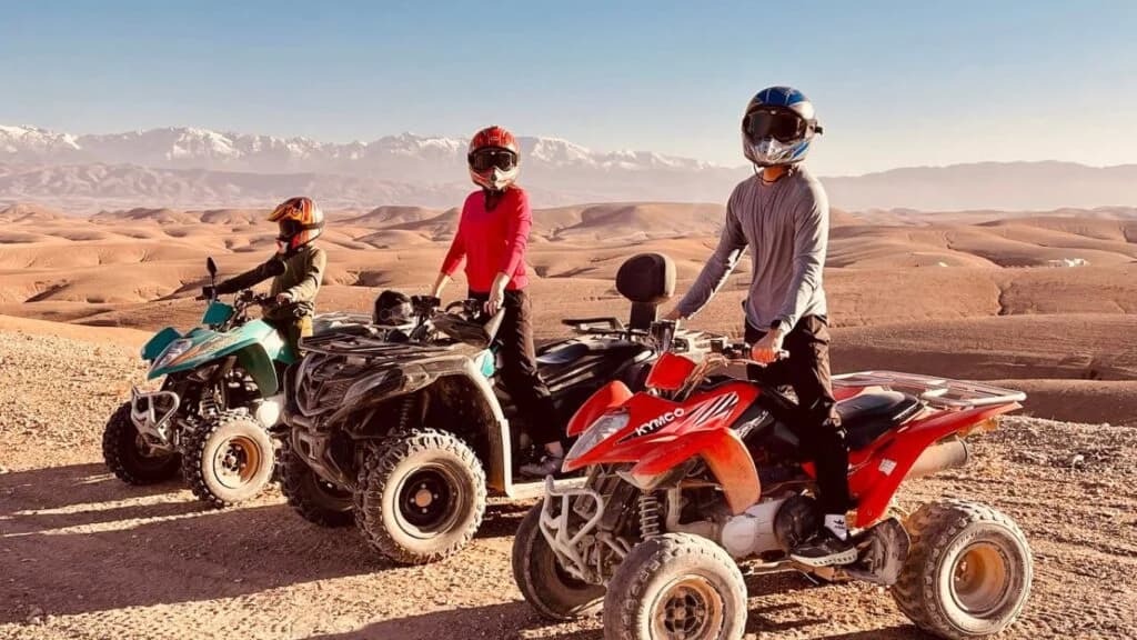 Riders standing with their quad bikes on a desert ridge overlooking the snow-capped Atlas Mountains