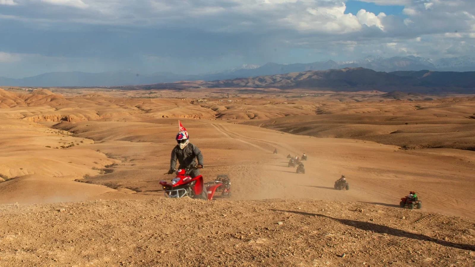 Convoy of quad bike riders following a ridge trail through the Agafay Desert at golden hour