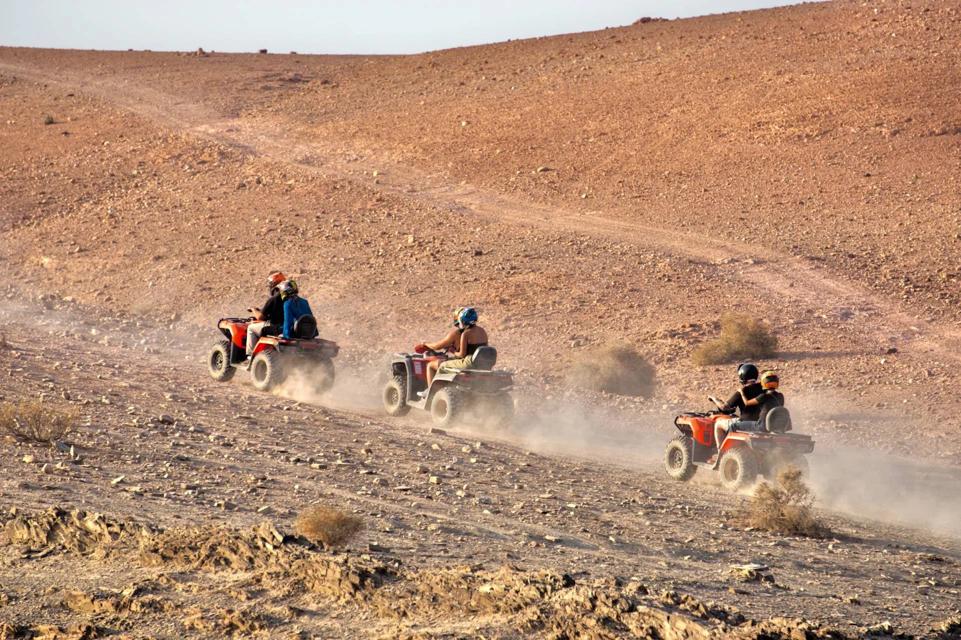 Three quad bikes with riders in a dusty desert bowl at golden hour