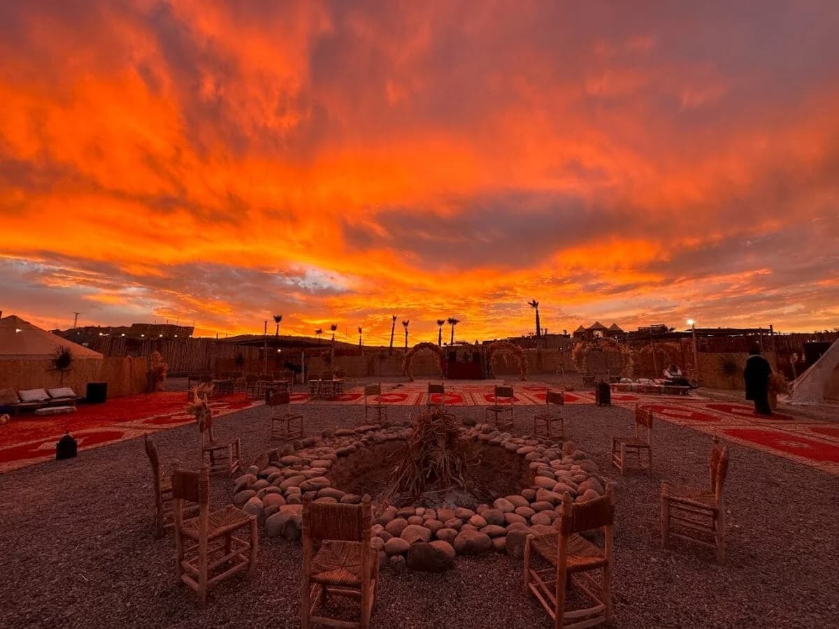 Dramatic sunset sky over a desert camp with a fire pit and decorative arches