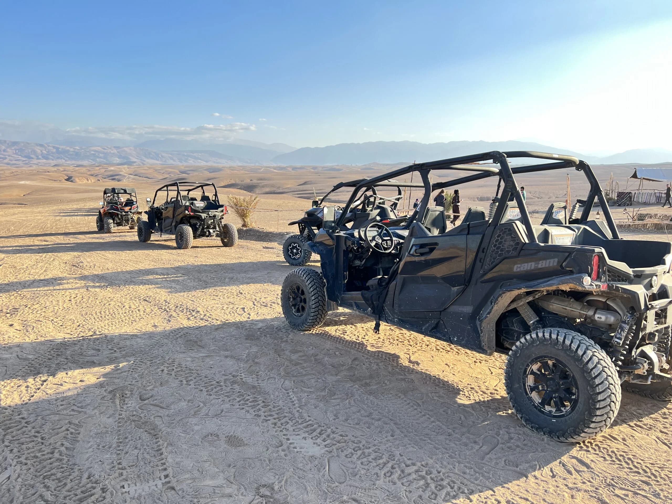 Several buggies parked at a desert camp in the Agafay Desert with mountains in the distance