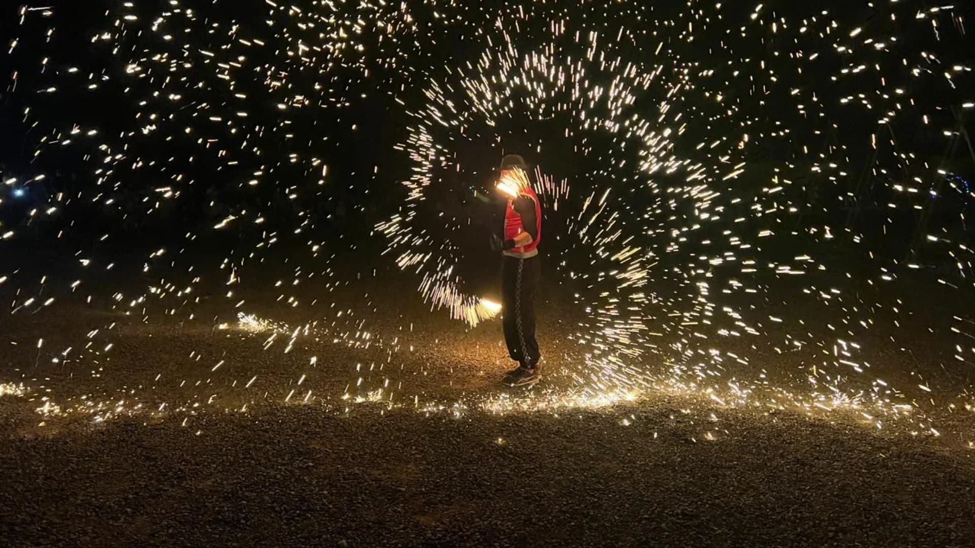 Fire performer spinning fire with sparks flying against the night sky
