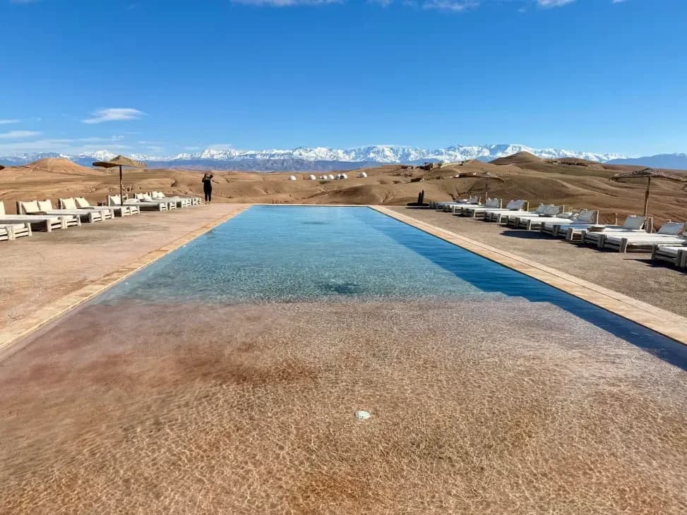 Desert camp pool with the snow-capped Atlas Mountains visible in the distance
